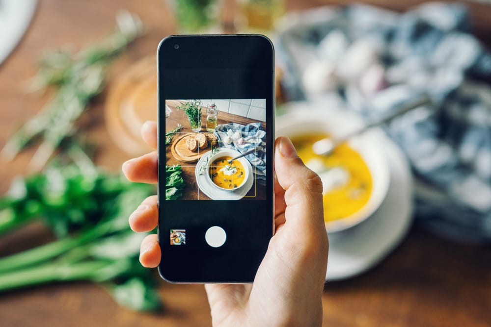 Persona sosteniendo un móvil haciendo una foto a un plato de comida